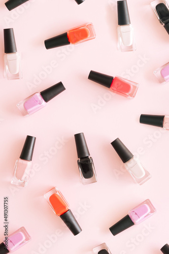 Nail polish in various colors on a pastel pink background. Aesthetic cosmetic fashion concept.