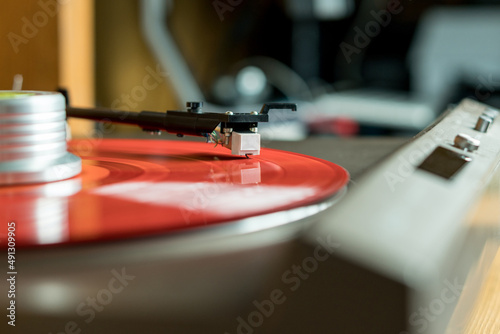 Closeup view of a tonearm and turntable playing color red vinyl record.