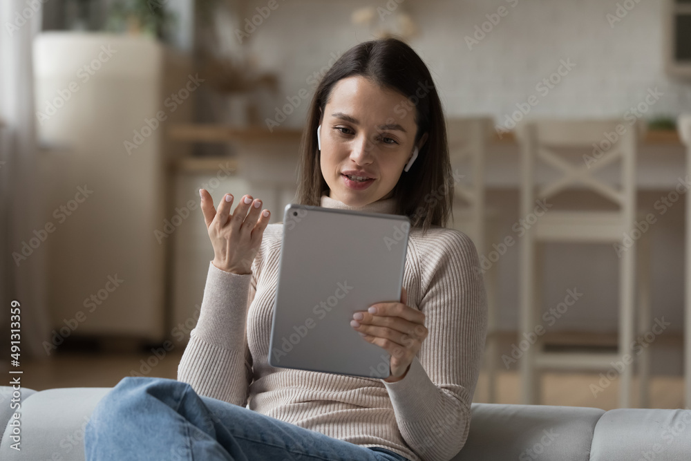 Woman sit on cozy sofa wear wireless earphones take part in video call event, communicates via videoconference app of digital tablet. Young gen use modern tech for remote talk, virtual meeting concept Woman sit on cozy sofa wear wireless earphones take part in video call event, communicates via videoconference app of digital tablet. Young gen use modern tech for remote talk, virtual meeting concept