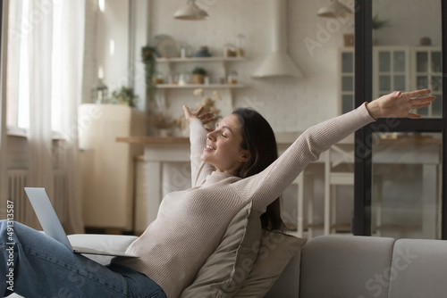Fototapeta Happy young woman relaxing alone on cozy sofa put wireless computer on laps, rai