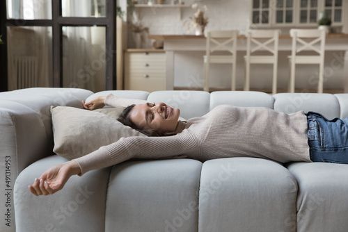 Carefree young woman stretching lying on comfortable couch in living room feeling peaceful, spend weekend leisure at home. Breath fresh conditioned air, enjoy cozy furniture at own or rented apartment