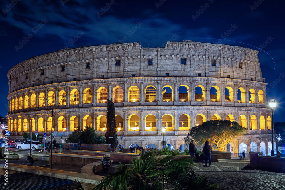 Night view of the Colosseum illuminated with warm yellow light, against the background of the blue sky of a cold winter night.