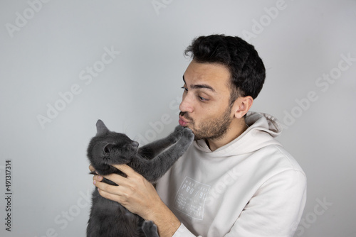 Young man holding and kissing cat on gray isolated background. Care and maintenance of pets.