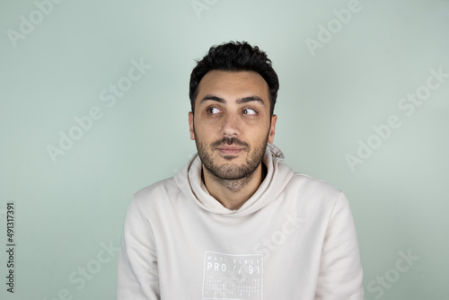 Close up portrait of young handsome boy in casual clothes posing for college photo, smiling, looking up with happy and thoughtful facial expression. Friendly gesturing on green background.
