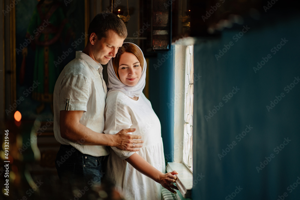 man and woman in headscarf and light-colored robes by window in church. man and woman in headscarf and light-colored robes by window in church.