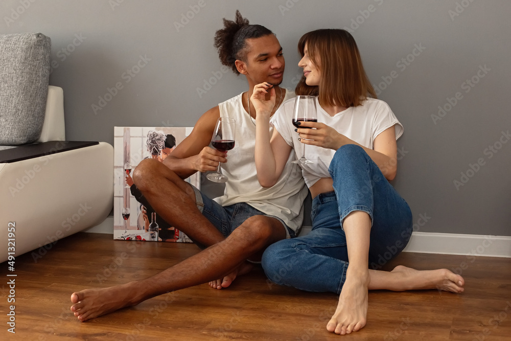 Stylish, modern, multiracial couple, a guy and a girl , sit at home on the floor against a gray wall