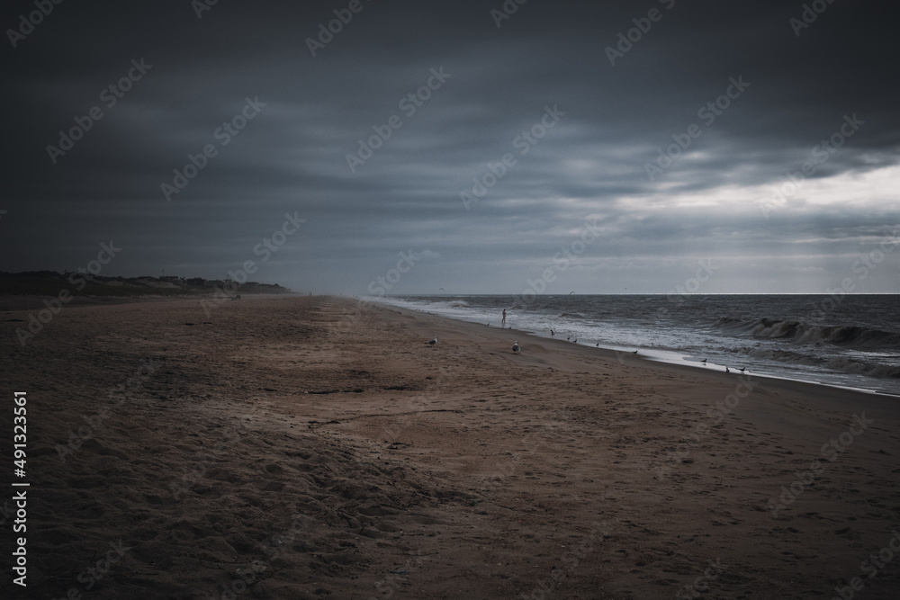 A man wades alone into the ocean on the beach at sunrise on a stormy day.