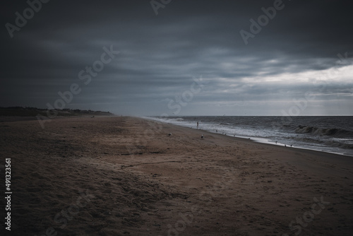 A man wades alone into the ocean on the beach at sunrise on a stormy day.