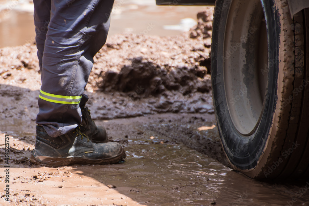 person standing on muddy asphalt next to a wheel of a vehicle