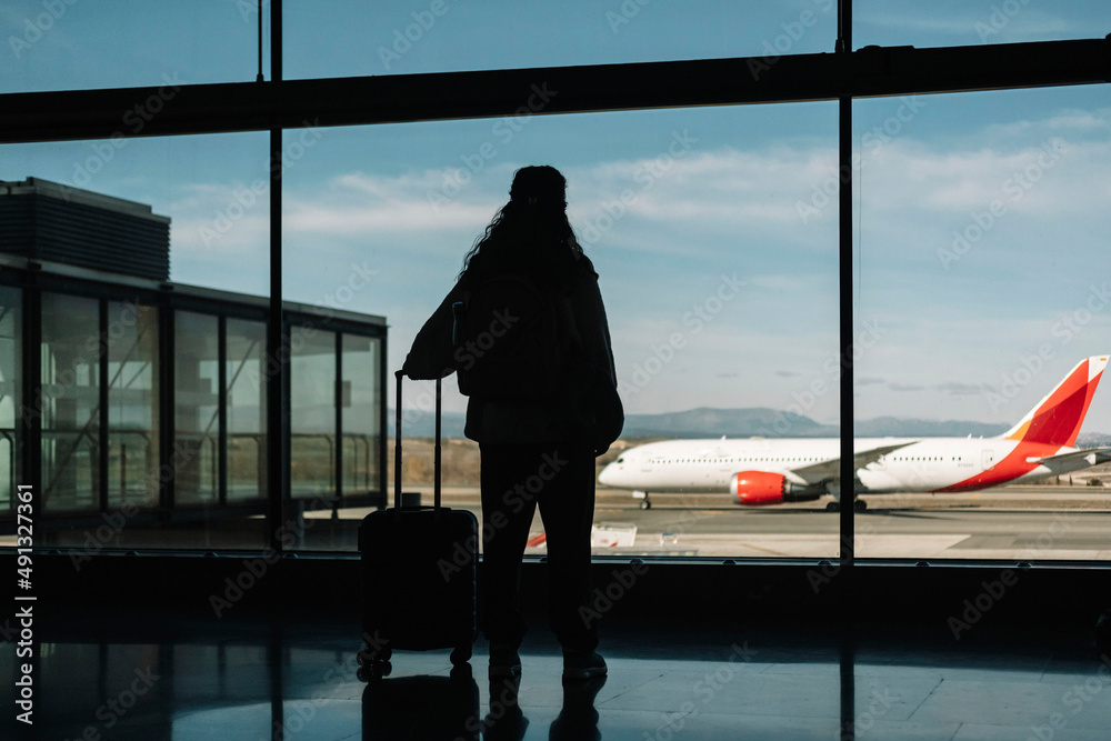 Silhouette of a woman with her luggage looking out the window at an airport. Travel concept. Silhouette of a woman with her luggage looking out the window at an airport. Travel concept.