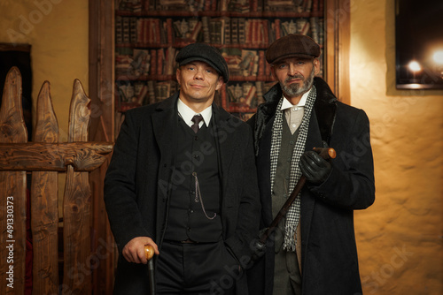 Foto Two men of different ages, English retro gangster of the 1920s dressed in a coat, suit and flat cap in Peaky blinders style
