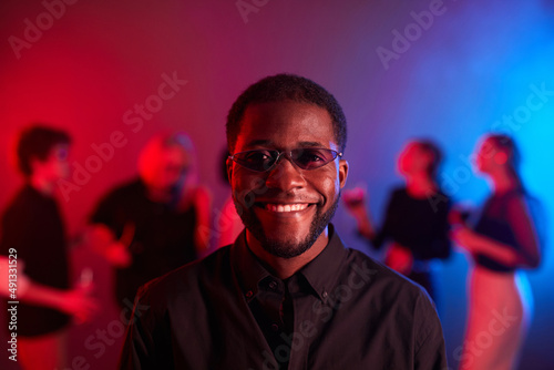 Front view portrait of African American man smiling at camera at party and wearing colored glasses in neon light