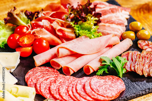 Assortment of salami prosciutto meats and sausages, olives and spices.Meat appetizer.Different types of sausages with tomatoes served on black table, flat lay.Top view.Healthy food concept.Copy space.