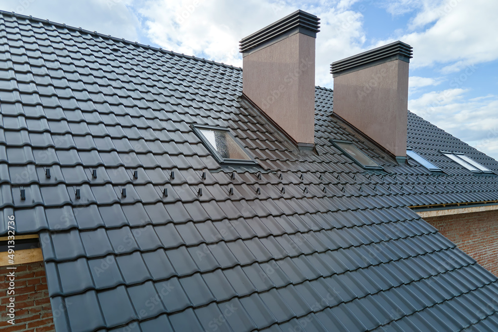 Closeup of attic windows and brick chimneys on house roof top covered with ceramic shingles. Tiled covering of building Closeup of attic windows and brick chimneys on house roof top covered with ceramic shingles. Tiled covering of building