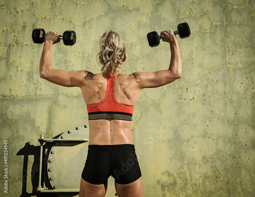 Rear view of athlete woman exercising with dumbbells photo