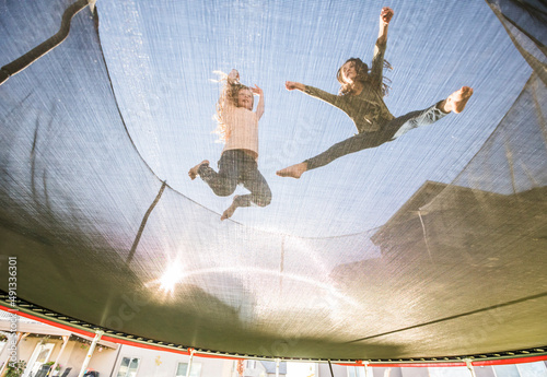 Low angle view of sisters (10-11, 12-13) jumping on trampoline photo