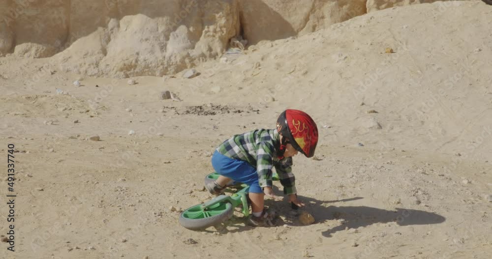 Back view of child toddler picking up bike after fall in dirt sandy terrain, day Back view of child toddler picking up bike after fall in dirt sandy terrain, day