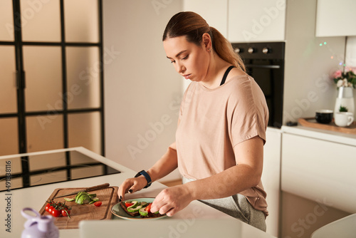 Beautiful young woman with prosthesis arm preparing food in modern kitchen