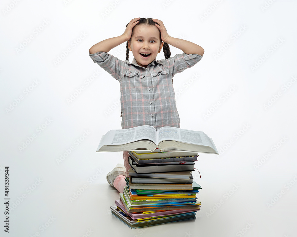 charming little girl is sitting in front of a large stack of books and has her head in her hands in surprise charming little girl is sitting in front of a large stack of books and has her head in her hands in surprise