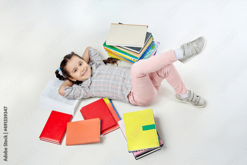 charming little girl with braided pigtails in the studio on a white background, a lot of books are scattered around her