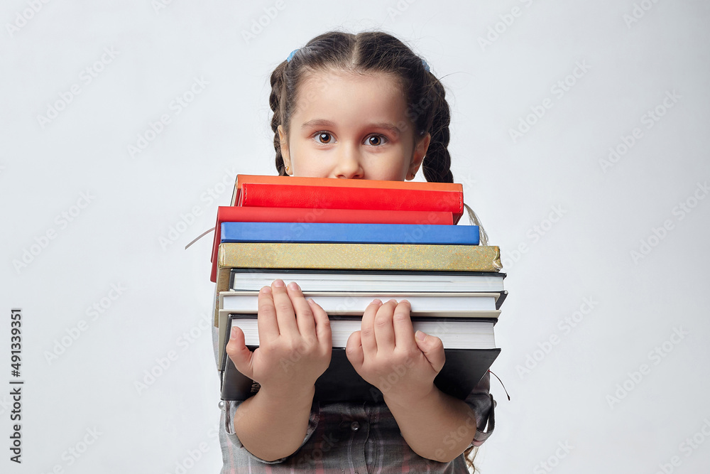little girl holds a large stack of books in front of her. photo shoot in the studio on a white background little girl holds a large stack of books in front of her. photo shoot in the studio on a white background