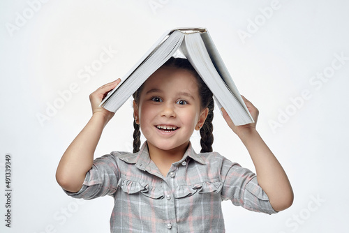 smiling little girl with braided pigtails holds a large book over her head