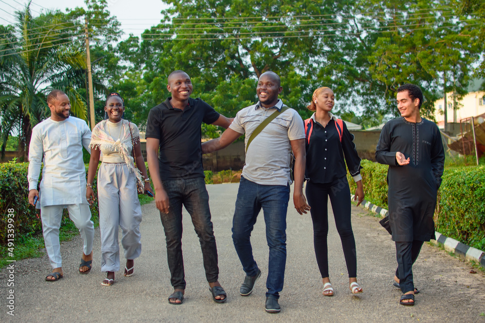Fototapeta premium Groups of african friends or students consisting of male and female individuals, happily chatting together as they stroll or walk along a tiled road in a school environment