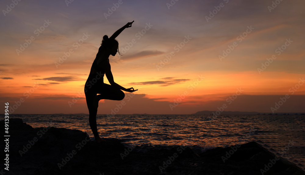 Silhouette Young woman practic Yoga during sun set on Rod on Coast ,  Slim and Healthy woman exercise by Yoga against sun set sky , Health lifestyle at outdoor