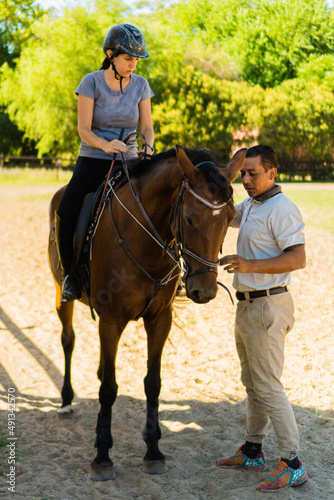 riding instructor teaching the sport to a young latina woman on top of a horse, vertical photo