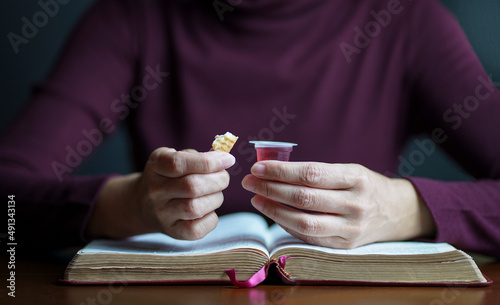 Εκτύπωση καμβά Woman holding biscuit and cup of wine with an open Bible on top of table, Taking Christian Holy Communion concept