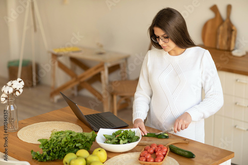 Portrait of a pregnant woman in the kitchen with a laptop on the table