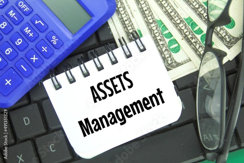 calculators, banknotes, glasses and notebooks with the word assets management