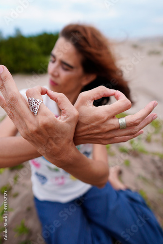 Latin female holds fingers in mudra gesture while meditates at the beach receiving spring season. Relaxation, spiritual, harmony and nature connection concept.