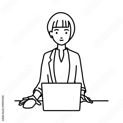 デスクで座ってPCを使っているジャケットの女性