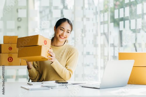 Portrait young attractive asia female owner startup business  work happy with box at home prepare parcel delivery in sme supply chain, procurement, omnichannel commerce online concept. photo