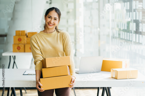 Young business woman working online e-commerce shopping at her shop. Young woman seller prepare parcel box of product for deliver to customer. Online selling, e-commerce. photo