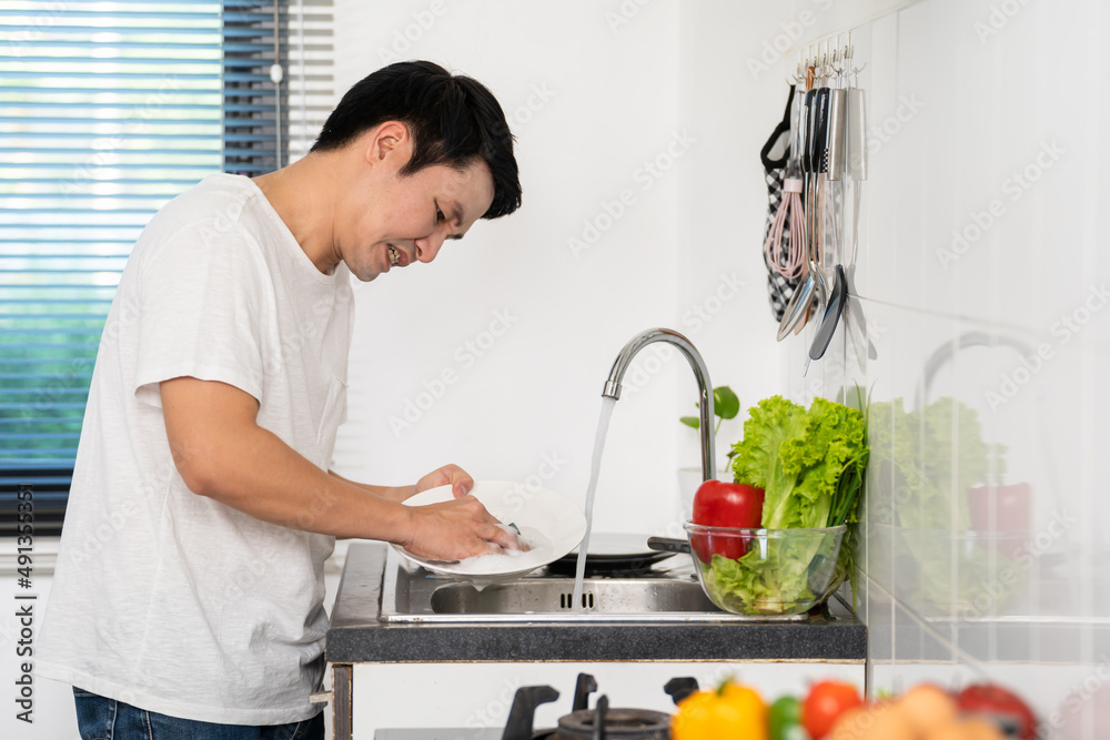 tired man washing dishes in the sink in kitchen at home tired man washing dishes in the sink in kitchen at home