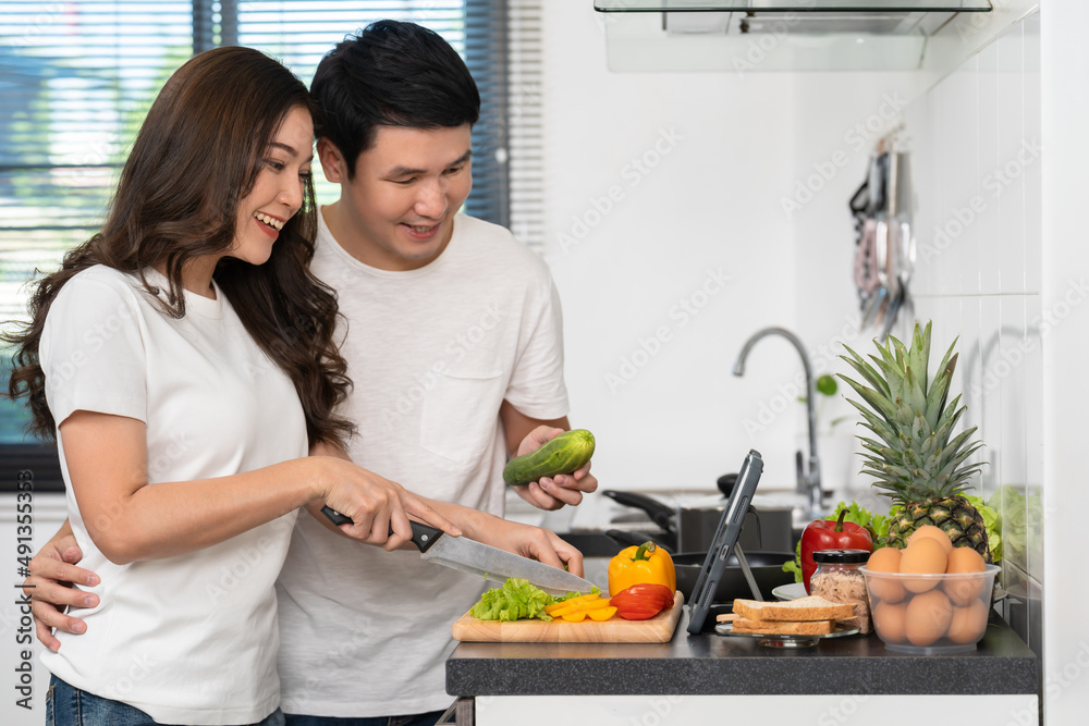 couple cooking and preparing vegetables according to a recipe on a tablet computer in kitchen at home couple cooking and preparing vegetables according to a recipe on a tablet computer in kitchen at home