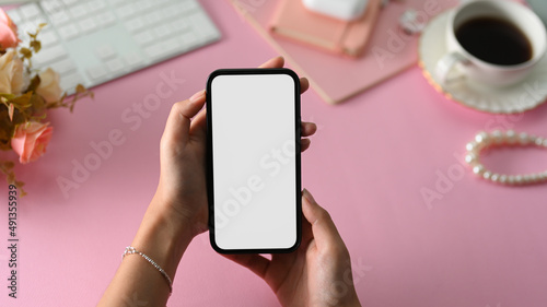 Female beauty blogger holding a mobile phone over her girly pink office desk.