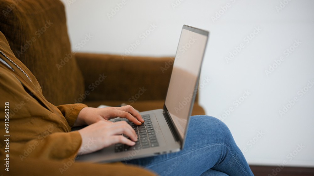 Fototapeta premium Side view, Female sits in comfortable sofa and working on laptop