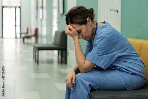 Quadro em tela Young tired or stressed female doctor in uniform sitting in hospital corridor wi
