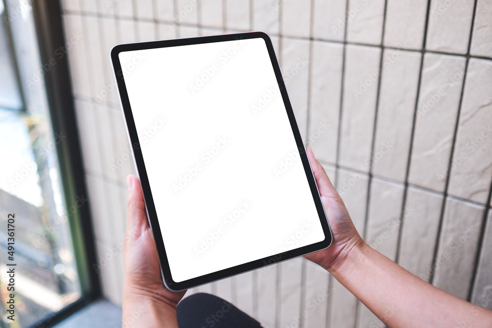 Mockup image of a woman holding digital tablet with blank white desktop screen in cafe