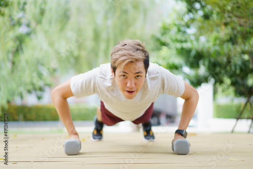 Active Asian sportsman making a body weight exercise, man doing push up workout with dumbbell. 