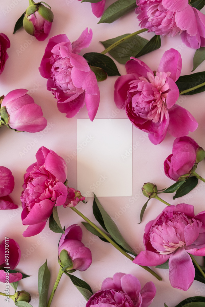 Blank paper invitation card with copy space. Pink peony flowers bouquet on neutral pastel elegant pink background. Flat lay, top view minimal floral composition