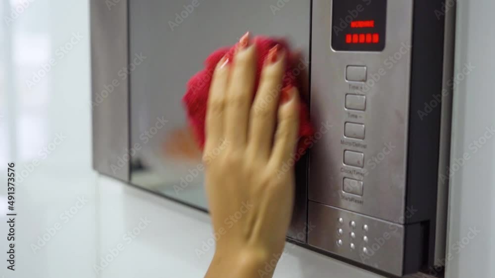 Woman use rag and spray to clean a microwave oven Woman use rag and spray to clean a microwave oven