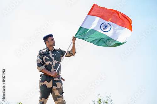 Indian army soldier holding waving Indian flag on top of mountain - concept of independence or repubilc day celebration, patriotism and pride photo