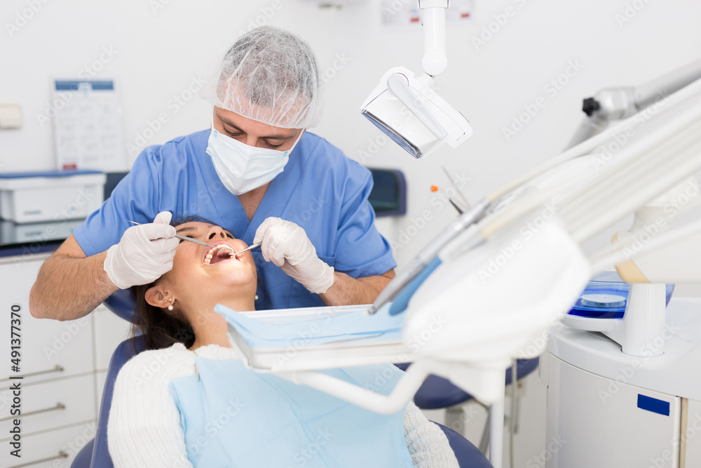 Fototapeta premium Portret of male dentist and woman patient sitting in medical chair during checkup at dental clinic office