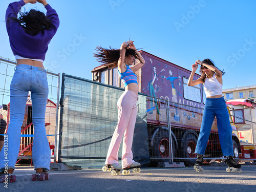 Three friends dancing wearing skates in the street next to a circus in a sunny day