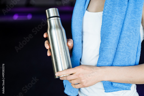 A bottle of water against the background of the girl's athletic body. Drinking regimen during exercise. A blue towel hangs around my neck. Thermos with hot tea. energy drink.