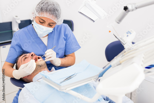 Professional dentist woman inspects patient teeth with dental tools - mirror and probe